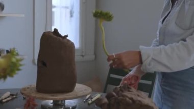 Yetenekli bir kadın seramikçi parlak bir atölyede sihrini gösterirken sanatsal yaratılış sürecine tanık olun. Dağınık malzeme ve aletlerle süslenmiş bir masanın önüne yerleştirilmişti.