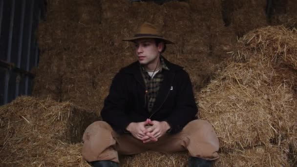 帽子をかぶった農夫の肖像 彼は干し草の上に座り 仕事の服を着ている ラテン系カウボーイ 労働者の肖像画 田舎の男 農業とハードマニュアル労働 人は自分自身で働く — ストック動画