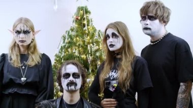 Dört kişi dekore edilmiş bir Noel ağacının önünde duruyor, her biri dramatik siyah beyaz yüz boyalarıyla, gotik veya fantezi karakterlerine benziyorlar. İki kadın siyah giyer, birinin elf kulakları vardır.