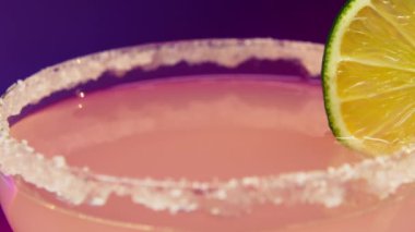Canlandırıcı Kokteyl Hazırlama: Tuz-Rimmed Glass 'a Lime ile Mor Arkaplanda Süt Dökülüyor. Süt, tuzlu ve limon dilimli bir kokteyl bardağına dökülüyor.