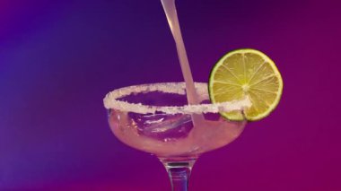 Canlandırıcı Kokteyl Hazırlama: Tuz-Rimmed Glass 'a Lime ile Mor Arkaplanda Süt Dökülüyor. Süt, tuzlu ve limon dilimli bir kokteyl bardağına dökülüyor.