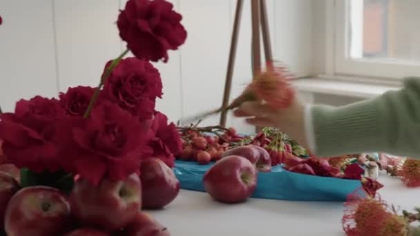 花屋の芸術 ヴィヴィッド レッド ローズとアップル アレンジメントを制作する 焦点を当て 芸術的な 緑のセーターの人は新鮮なりんごによって補完される緑の赤いバラとの花の配置を作成します — ストック動画