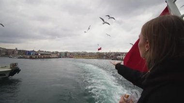 Sahne bir feribotta çekiliyor ve bir şahıs elinde belirgin bir hilal ve yıldızla büyük bir ulusal bayrak tutuyor. Rüzgarda dalgalanan bayrak, gri bulutlarla dolu bir arka planda
