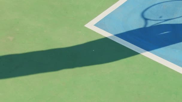 テニスプレーヤーの中間アクションの影は ハードコートの明るい青い表面に鋭く投げられ 白い線とサービスボックスを示す明るい青い領域に囲まれています プレイヤーが作ったものではありません — ストック動画