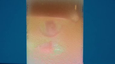 Bir kristal berrak cam, fokurdayan şeftali renkli soda ile dolu, çarpıcı mavi bir arka plana karşı duruyor. Karbonatlı içeceğin coşkusu yavaş yavaş azalıyor.