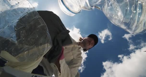 ビデオは 彼がプラスチックボトルと廃棄物を収集するように エコロジカルなクリーンアップに従事している男性を示すユニークな地上レベルの視点を提供しています 明るく輝く太陽 キャスティングレイ そして — ストック動画