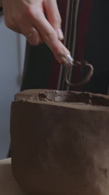 Bu dikey video çerçevesi, bir atölye ortamında çömlek çarkında killeri şekillendiren bağımsız bir sanatçının ellerini yakalıyor. Elleri becerikli ve odaklı, kullanılabilir materyalleri manipüle ediyor.