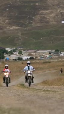 Görüntü, tozlu, dolambaçlı bir dağ yolunda ilerlerken hız ve macera tutkularıyla birleşen üç motosikletliyi gösteriyor. Dinamik sahne engebeli bir araziye göre ayarlanmış.