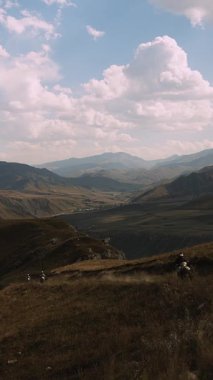 Bu büyüleyici kare, yüksek bir dağ yolunda seyahat eden iki motosikletliyi yakalıyor. Bisikletleri muhteşem bir tepe ve vadi zeminine toz püskürtüyor. Geniş gökyüzü