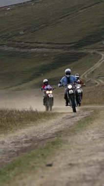 Görüntü, tozlu, dolambaçlı bir dağ yolunda ilerlerken hız ve macera tutkularıyla birleşen üç motosikletliyi gösteriyor. Dinamik sahne engebeli bir araziye göre ayarlanmış.