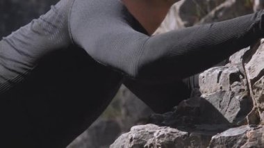 Yakın çekim, kaya tırmanışının fiziksel gerginlik ve konsantrasyonunu gösteren sert bir taş yüzeyini kavrayan bir dağcının gergin eline odaklanır. Konu, muhtemelen genç bir çocuk.
