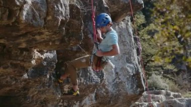 Koruyucu mavi kask takan bir kaya tırmanışçısı bir kayalıktan tırmanma ipine iniyor. Profesyonel bir dağcı dağlık bir bölgede cankurtaran olarak çalışır. Yüksek kalite 4k görüntü