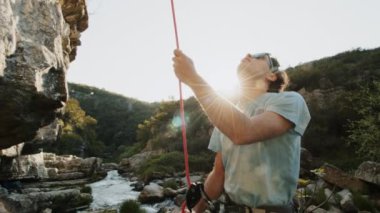 Bir dağcı yukarı bakar, yükselmeden önce rotayı belirler. Güneş arkamızda parlıyor, kanyonların kayalık köşelerinde parıldıyor. Güneş gözlüğü ve günlük giysiler sıcak ve aydınlık bir gün olduğunu gösteriyor. Dağcılar.