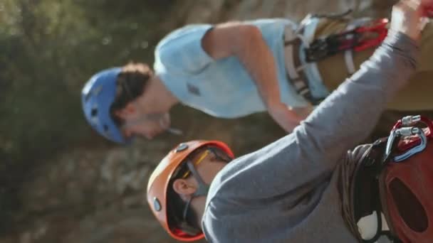 一組の登山者は 頑丈な崖の背景に対して装置をチェックします 彼らは注意深く ヘルメットとハーネスが確保されています この画像は パートナーシップと安全チェックの瞬間をキャプチャします — ストック動画