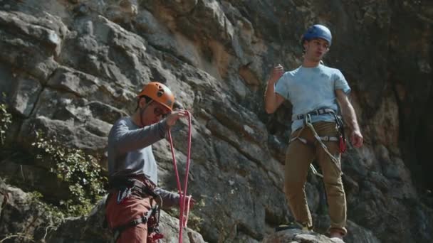 一組の登山者は 頑丈な崖の背景に対して装置をチェックします 彼らは注意深く ヘルメットとハーネスが確保されています この画像は パートナーシップと安全チェックの瞬間をキャプチャします — ストック動画