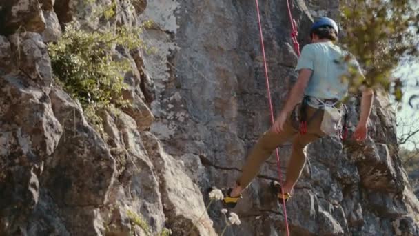 Prores の撮影は 石灰岩の崖のテクスチャーされた背景に対する岩石の登山者の意図的な降下を捉えています クライマー しっかりとハーネスされ 岩の表面をラッパー ガイド付き — ストック動画
