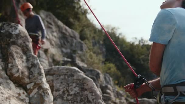One Climber Secures Rope While Another Ascends Rocky Cliff Focus — Stock Video