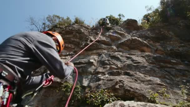 这张照片拍摄的是一个穿着烧焦的橙色头盔的登山者 他全神贯注地管理着一个系带系统 攀登者用经验丰富的手抓起粉红色的攀爬绳 确保安全稳妥 — 图库视频影像