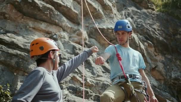 崖の上の2人の登山者が一緒に働いている 一つは もう一つにロープを与えている ヘルメットやハーネスを着用しています 背景には岩と空がある 高品質の4K映像 — ストック動画