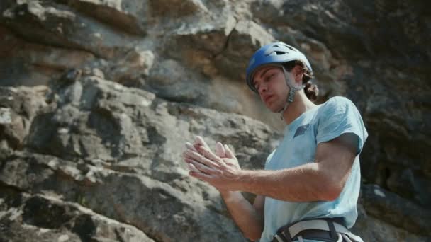 男性のロッククライマーが岩に登ろうとしています 彼は手をひねって チョークダストは彼らから来ます 青いヘルメットを着ています 達成の概念 — ストック動画