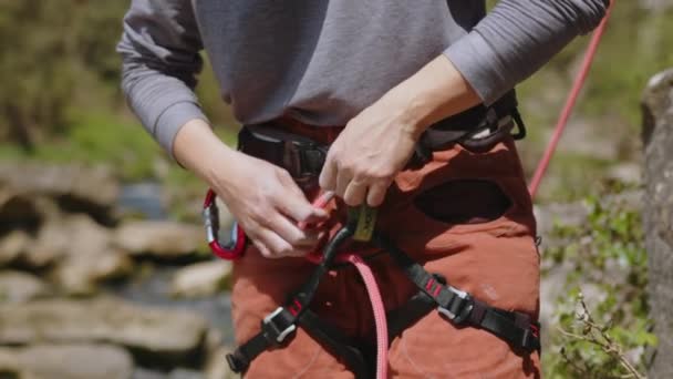 岩を登る準備をしている女性運動ロッククライマー 崖の下のハーネスでロープノットをチェックしている女性は登る準備をしています 高品質の4K映像 — ストック動画