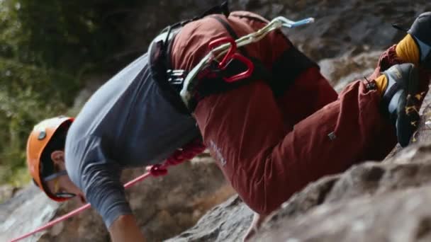 このダイナミックなイメージは 急な岩の顔の上に2人の登山者を示しています 焦点は 前景の1つのクライマーにあり 彼の機器と彼の筋肉の緊張に細心の注意を払っています — ストック動画