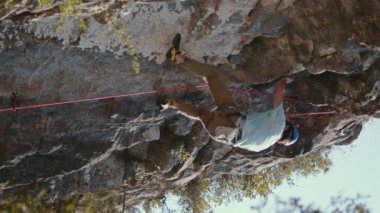 Bir dağcının tepetaklak görüntüsü, sahnenin heyecanını ve meydan okumasını arttıran bir şaşkınlık hissi yaratıyor. Açık gri gömlek ve taba rengi pantolon giyen dağcı ileri teknoloji kullanır.