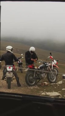 Bu dikey çerçeve, off-road bisikletlerinin yanında tam teçhizatlı iki motosikletliyi bir yolculuğa çıkmaya hazır halde yakalar. Ön plana bir aracın arkası hükmediyor ve bir çerçeve oluşturuyor.