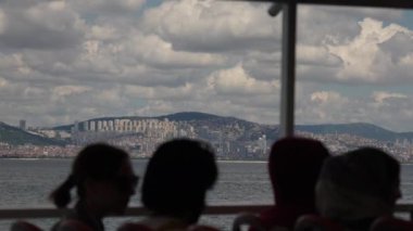 İstanbulların geniş şehir manzarasının yavaş çekim görüntüsü, Boğaz 'da bir feribot turundan alındı. Ön planda, çevre ışıklarıyla kısmen aydınlatılmış yolcu siluetleri,