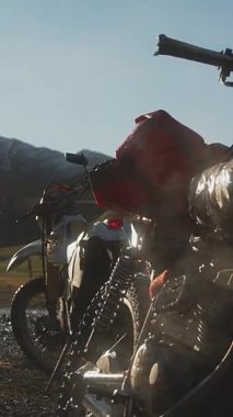 İki off-road motosikleti toprak bir yolda park halindedir ve sabahın erken saatlerinde sis yükselir. Motorlar, zincir ve şok emiciler gibi ayrıntılı parçalarıyla arka planda vurgulanmış.