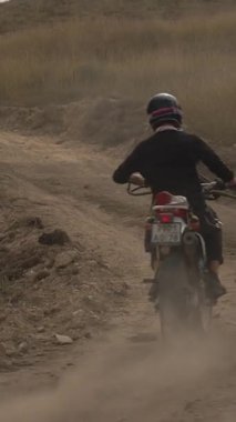 Yalnız bir motosikletçi, tozlu bir tepede off-road yolunda ustalıkla engebeli arazide geziniyor. Kasklı ve siyah kıyafetli sürücü, patikadan çıkarken arkadan yakalanır.
