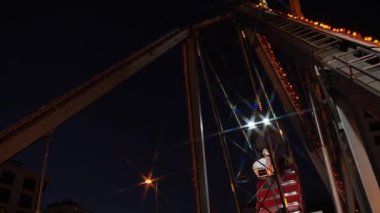 Gece vakti bir lunaparkta dev bir salıncak hareket halinde. Işıklar karanlık gökyüzüne karşı yapıyı aydınlatıyor. Sahne, sürüşün dinamik salınımlarını yakalar ve bir his yaratır.