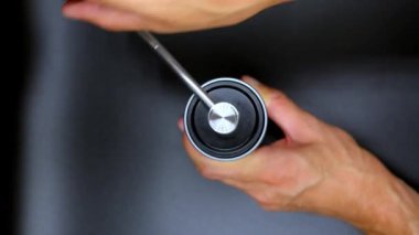 Yukarıdan aşağıya bakıldığında, parlak metal saplı el yapımı kahve öğütücüsü kullanan bir kişi görülüyor. Eller, öğütücünün hassasiyetini ve işlevselliğini vurgulamak için kolu dikkatlice çeviriyor. Şey...