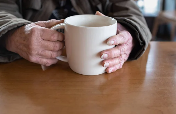 Old woman holding cup of hot coffee drink in her hands. Close up of an elderly woman\'s hand holding a cup of tea or coffee. Copyspace for text, selective focus