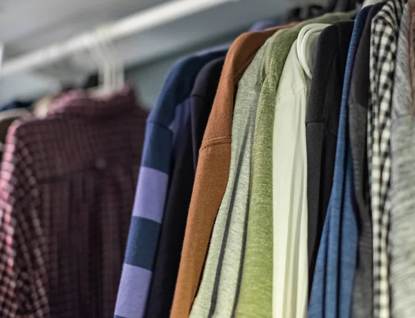 Mens wardrobe clothing hanging on rail in closet. Closeup photo of Men's shirts and sweaters hanging on a rack. Wardrobe clothing hanging on rail in closet. Nobody, selective focus