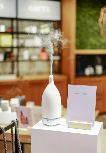 Modern aroma oil diffuser on a stand. Electric Essential oils Aroma diffuser. Ultrasonic aromatherapy oil diffuser in use. Atomized water droplets being dispensed into the air.