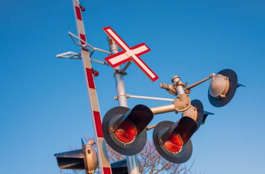 Railroad crossing traffic sign with red lights and barrier lowering indicating that a train is coming. Railroad crossing sign against blue sky background, copyspace for text, street photo
