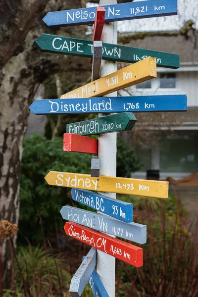 Colorful wooden direction arrow signs on wooden poles. Direction to different places of the world indicated in a street sign. Multiple wooden arrow signposts on wood pole on a street in Canada