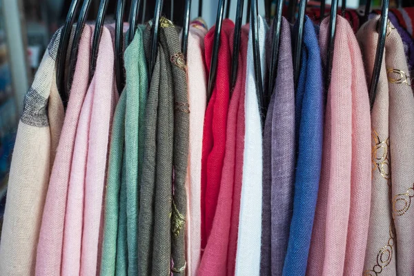 Clothes color on a clothes rack. Row of different colorful womens textiles on a hanger. A lot of scarfs of different colors on a hanger. Nobody