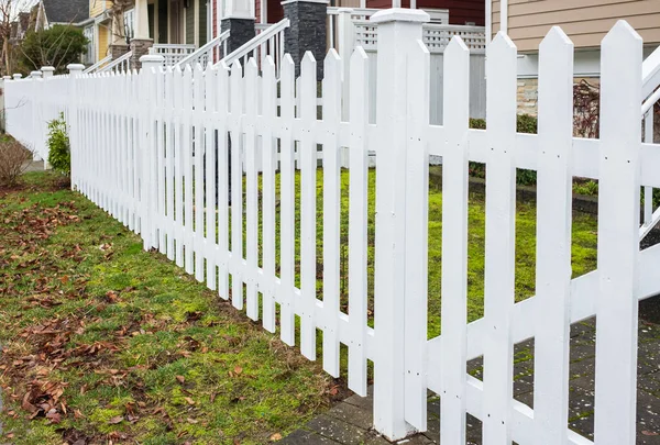Nice wooden fence around house. Wooden white fence with green lawn. Street photo, nobody, selective focus