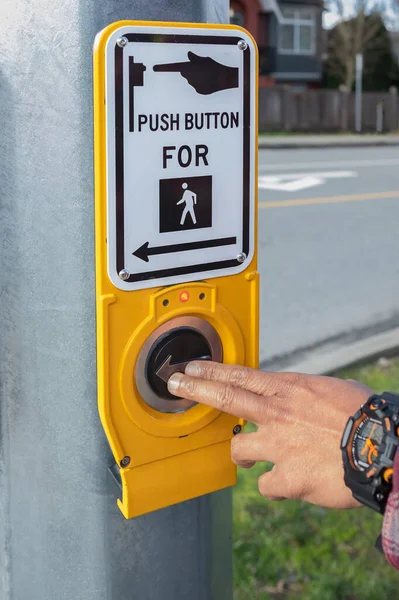 Hand pressing a button at traffic lights on pedestrian crossing. Pushing button for traffic light. Button of the mechanism lights traffic lights on the street. System control traffic light