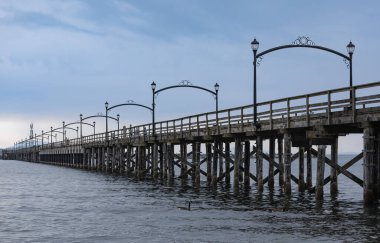 Wooden pier at White Rock, BC, Canada extends diagonally into image. Wooden Pier Walk during a cloudy sunset. Travel photo, selective focus