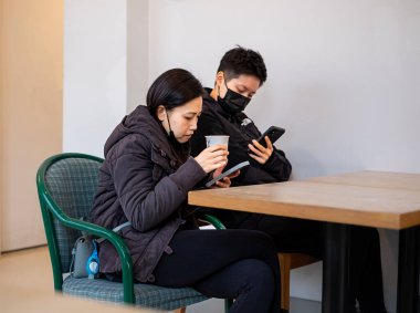Young Asian couple using smartphones at cafe. Asian couple having coffee and watching on theirs smart phones. Information technology, cafe lifestyle. Vancouver BC Canada-January 23,2023