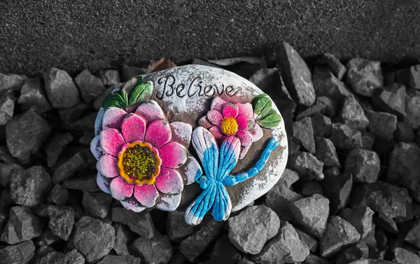 Painted rock with words of encouragement. Believe painted on a rock with flowers. Rock with painted A motivational encouraging message held. Nobody, selective focus