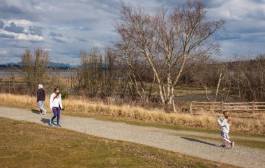Gülümseyen orta yaşlı bir kadın, kıdemli bir bayan ve sonbahar parkında yürüyen küçük bir kız. Aktif insanlar yürüyorlar ve güneşli sonbahar gününün tadını çıkarıyorlar - Vancouver Kanada-7 Mart 2023-Sokak fotoğrafı