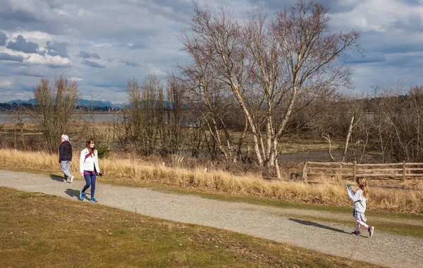 Gülümseyen orta yaşlı bir kadın, kıdemli bir bayan ve sonbahar parkında yürüyen küçük bir kız. Aktif insanlar yürüyorlar ve güneşli sonbahar gününün tadını çıkarıyorlar - Vancouver Kanada-7 Mart 2023-Sokak fotoğrafı