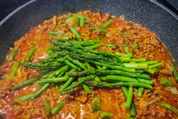 Pan with freshly cooked ground meat and asparagus, top view. Stir Fry meat with onion, tomatos, garlic, chili and asparagus. Asian food. Nobody, selective focus