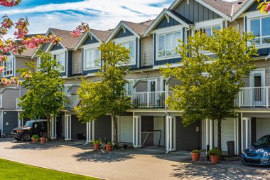 Güneşli bir günde güzel bir mahalle. Kasaba evleri için park yerindeki garaj kapılarında sıra var. Beton garaj yolu, garaj kapısı ve penceresi olan evin dışı. Garaj kapısı, kısa yol.