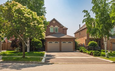 Güneşli bir günde gayrimenkul paravanı. Yazın banliyölerde bahçe ve garaj yolu güzel döşenmiş lüks evler. Bahçeli güzel bir ev girişi.