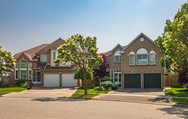 Real Estate Exterior Front House on a sunny day. Big custom made luxury houses with nicely landscaped front yard and driveway to garage in summer in the suburbs. Beautiful house entrance with a garden